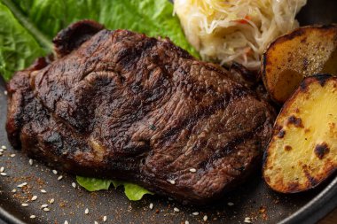 Fırında altın patatesli ızgara biftek. Ekşi lahana ve koyu arkaplanda kırmızı sosla servis ediliyor. Lezzetli yemek tarifi. Akşam yemeğinde tavada pişirilmiş domuz filetosu. Kızarmış Sulu Et Dokuları.