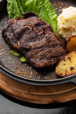 Fırında altın patatesli ızgara biftek. Ekşi lahana ve koyu arkaplanda kırmızı sosla servis ediliyor. Lezzetli yemek tarifi. Akşam yemeğinde tavada pişirilmiş domuz filetosu. Kızarmış Sulu Et Dokuları.