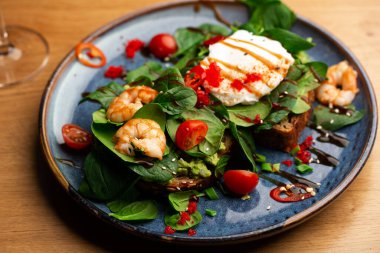 Haşlanmış yumurtalı karabuğday ekmeği tostu, dilimlenmiş avokado, karides, domates ve marul. Beslenme menüsü. Düz yatıyordu