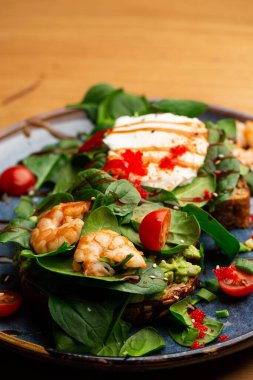 Haşlanmış yumurtalı karabuğday ekmeği tostu, dilimlenmiş avokado, karides, domates ve marul. Beslenme menüsü. Düz yatıyordu