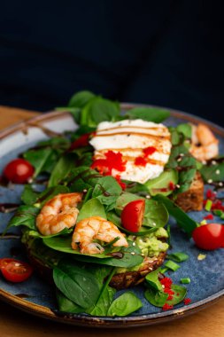 Haşlanmış yumurtalı karabuğday ekmeği tostu, dilimlenmiş avokado, karides, domates ve marul. Beslenme menüsü. Düz yatıyordu