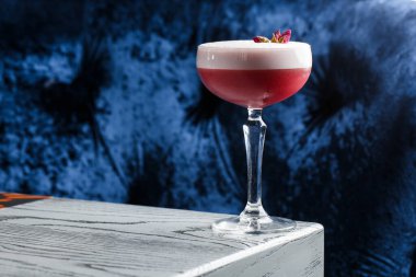 Pembe Yonca Kulübü Kokteylleri Coupe Glass 'ta Köpük tabakası ve karanlığa gömülmüş çiçek garnitürleriyle.