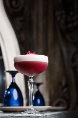 Pembe Yonca Kulübü Kokteylleri Coupe Glass 'ta Köpük tabakası ve karanlığa gömülmüş çiçek garnitürleriyle.