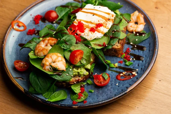 Haşlanmış yumurtalı karabuğday ekmeği tostu, dilimlenmiş avokado, karides, domates ve marul. Beslenme menüsü. Düz yatıyordu