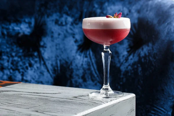 Pembe Yonca Kulübü Kokteylleri Coupe Glass 'ta Köpük tabakası ve karanlığa gömülmüş çiçek garnitürleriyle.