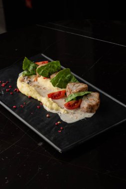 Beyaz tabakta garnitür olarak fırında et ve patates püresi. Makro yakın plan siyah arka plan. Lezzetli yemek, restoran menüsü konsepti