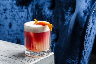 Klasik kırmızı kokteyl. Arka planda buz ve portakal kabuğu olan retro bardakta..