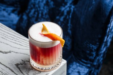 Klasik kırmızı kokteyl. Arka planda buz ve portakal kabuğu olan retro bardakta..