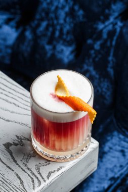 Klasik kırmızı kokteyl. Arka planda buz ve portakal kabuğu olan retro bardakta..