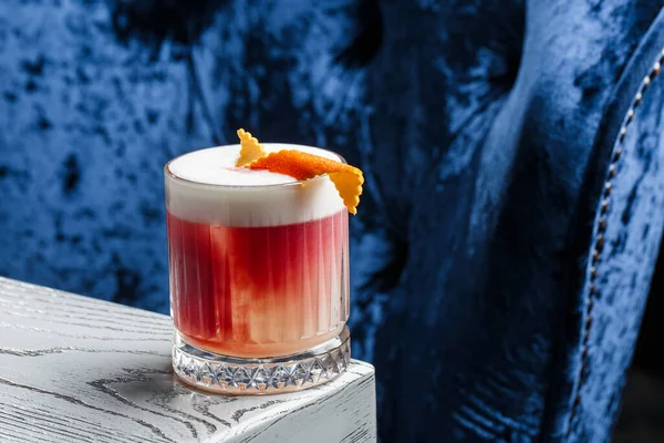 Klasik kırmızı kokteyl. Arka planda buz ve portakal kabuğu olan retro bardakta..