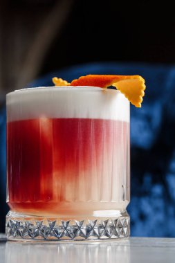 Klasik kırmızı kokteyl. Arka planda buz ve portakal kabuğu olan retro bardakta..