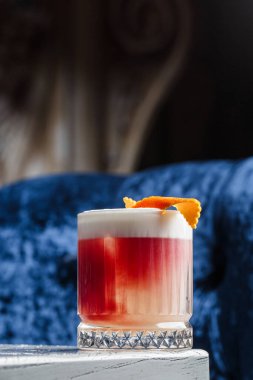 Klasik kırmızı kokteyl. Arka planda buz ve portakal kabuğu olan retro bardakta..