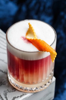 Klasik kırmızı kokteyl. Arka planda buz ve portakal kabuğu olan retro bardakta..