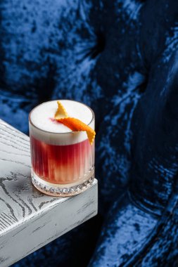 Klasik kırmızı kokteyl. Arka planda buz ve portakal kabuğu olan retro bardakta..