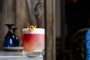 Klasik kırmızı kokteyl. Arka planda buz ve portakal kabuğu olan retro bardakta..