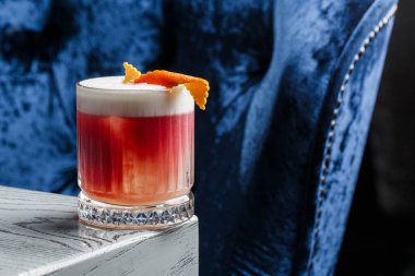 Klasik kırmızı kokteyl. Arka planda buz ve portakal kabuğu olan retro bardakta..