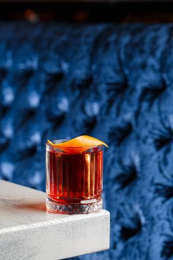 Parlak soğuk alkollü kristal bardak. Portakal suyuyla süslenmiş. Arka plan bulanık. Negroni kokteyli..