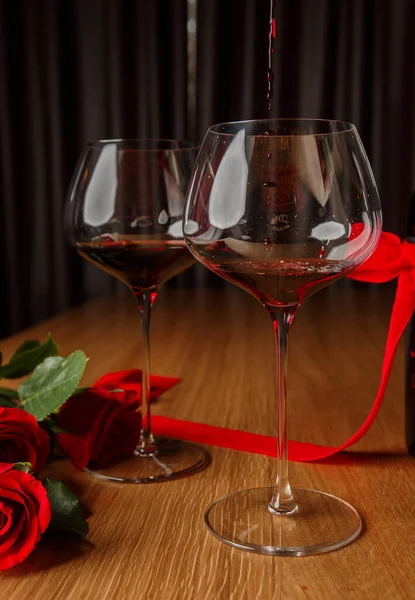 Romantik yemek. Masanın üzerinde duran bir buket çiçek, bir demet gül ve ahşap masada duran iki kadeh kırmızı şarap. Tarih kavramı, bulanık arkaplan, pankart, kopyalama alanı