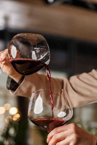 Мужская рука держит красивый прозрачный стебель для бордового вина, в которое наливают красное вино из другого стебля
