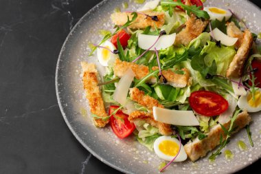 Izgara tavuk göğsü, marul, kızarmış ekmek, yumurta, vişneli domates, parmesan peyniri ve soslu Sezar salatası. Siyah bir arkaplanda izole edilmiş.