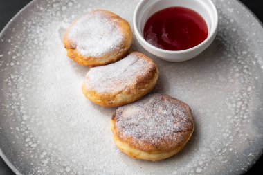 Süzme peynirli krep, Syrniki veya kırmızı soslu cheesecake, siyah mermer arka planda izole edilmiş. Ev yapımı yemek. Lezzetli bir kahvaltı. Seçici odak