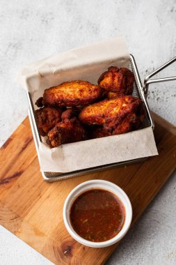 Gerçek sıcak barbekü sosuyla kaplanmış kızarmış tavuk kanatları mermer arka planda kesme tahtasında kırmızı acı biber sosuyla servis edilir.