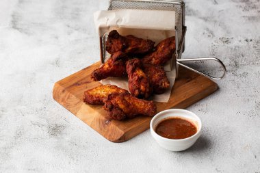 Gerçek sıcak barbekü sosuyla kaplanmış kızarmış tavuk kanatları mermer arka planda kesme tahtasında kırmızı acı biber sosuyla servis edilir.