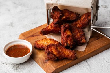 Gerçek sıcak barbekü sosuyla kaplanmış kızarmış tavuk kanatları mermer arka planda kesme tahtasında kırmızı acı biber sosuyla servis edilir.