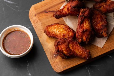 Gerçek sıcak barbekü sosuyla kaplanmış kızarmış tavuk kanatları mermer arka planda kesme tahtasında kırmızı acı biber sosuyla servis edilir.