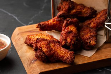 Gerçek sıcak barbekü sosuyla kaplanmış kızarmış tavuk kanatları mermer arka planda kesme tahtasında kırmızı acı biber sosuyla servis edilir.