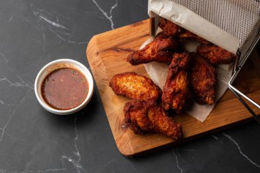 Gerçek sıcak barbekü sosuyla kaplanmış kızarmış tavuk kanatları mermer arka planda kesme tahtasında kırmızı acı biber sosuyla servis edilir.