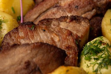 Fırında taze patates, deniz tuzu ve domuz filetosu ile mermer masada siyah bir tabakta parçalara ayrılmış.