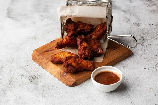 Gerçek sıcak barbekü sosuyla kaplanmış kızarmış tavuk kanatları mermer arka planda kesme tahtasında kırmızı acı biber sosuyla servis edilir.