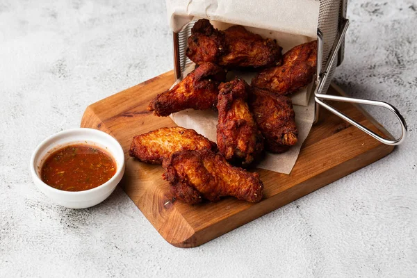 Gerçek sıcak barbekü sosuyla kaplanmış kızarmış tavuk kanatları mermer arka planda kesme tahtasında kırmızı acı biber sosuyla servis edilir.