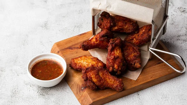 Gerçek sıcak barbekü sosuyla kaplanmış kızarmış tavuk kanatları mermer arka planda kesme tahtasında kırmızı acı biber sosuyla servis edilir.