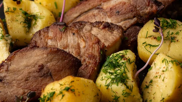 Fırında taze patates, deniz tuzu ve domuz filetosu ile mermer masada siyah bir tabakta parçalara ayrılmış.