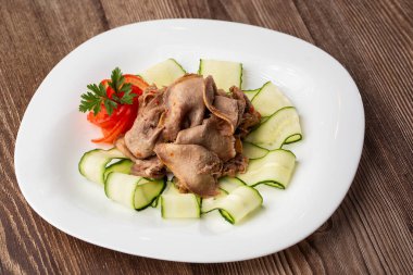 Restoran menüsünden yemek servisi. Dilimlenmiş sığır dili, ahşap zemin üzerinde salatalık, lezzetli bir aperatif..