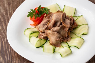 Restoran menüsünden yemek servisi. Dilimlenmiş sığır dili, ahşap zemin üzerinde salatalık, lezzetli bir aperatif..