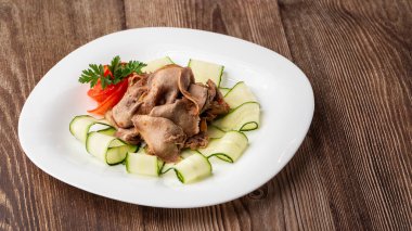 Restoran menüsünden yemek servisi. Dilimlenmiş sığır dili, ahşap zemin üzerinde salatalık, lezzetli bir aperatif..