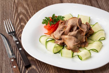 Restoran menüsünden yemek servisi. Dilimlenmiş sığır dili, ahşap zemin üzerinde salatalık, lezzetli bir aperatif..