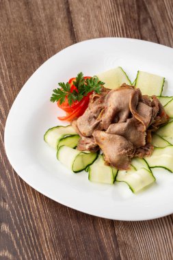 Restoran menüsünden yemek servisi. Dilimlenmiş sığır dili, ahşap zemin üzerinde salatalık, lezzetli bir aperatif..