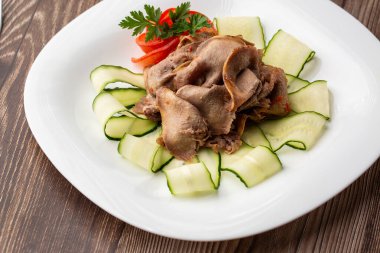 Restoran menüsünden yemek servisi. Dilimlenmiş sığır dili, ahşap zemin üzerinde salatalık, lezzetli bir aperatif..