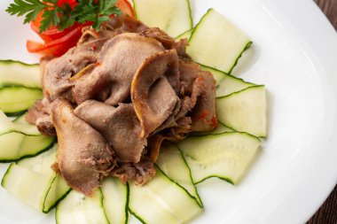 Restoran menüsünden yemek servisi. Dilimlenmiş sığır dili, ahşap zemin üzerinde salatalık, lezzetli bir aperatif..