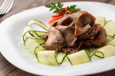 Restoran menüsünden yemek servisi. Dilimlenmiş sığır dili, ahşap zemin üzerinde salatalık, lezzetli bir aperatif..