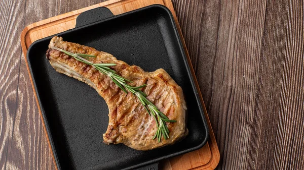 Roasted pork chop steak with spices and rosemary on black plate on wooden background. Pork, beef, chop on a bone. top view. place for text