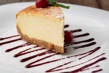 New York peynirli keki mi yoksa karamel kaplı klasik peynirli kek mi? Yakından bak. Lezzetli bir kahvaltı. Beyaz tabakta, ahşap zeminde bir parça kek.