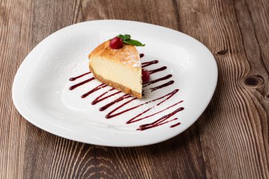 New York peynirli keki mi yoksa karamel kaplı klasik peynirli kek mi? Yakından bak. Lezzetli bir kahvaltı. Beyaz tabakta, ahşap zeminde bir parça kek.