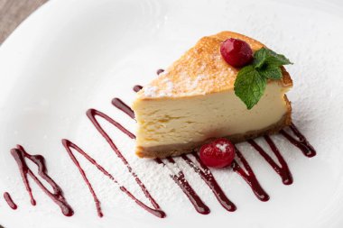 New York peynirli keki mi yoksa karamel kaplı klasik peynirli kek mi? Yakından bak. Lezzetli bir kahvaltı. Beyaz tabakta, ahşap zeminde bir parça kek.