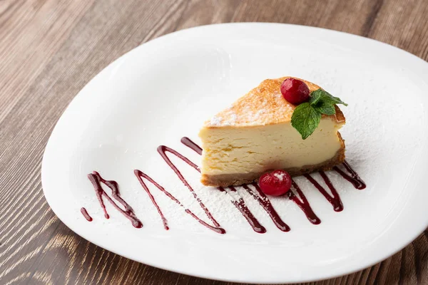New York peynirli keki mi yoksa karamel kaplı klasik peynirli kek mi? Yakından bak. Lezzetli bir kahvaltı. Beyaz tabakta, ahşap zeminde bir parça kek.