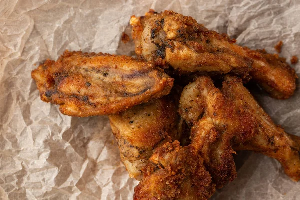 Hakiki sıcak barbekü sosuyla kaplanmış kızarmış tavuk kanatları. Ahşap arka planda parşömen kağıdında kırmızı acı biber sosuyla servis ediliyor.